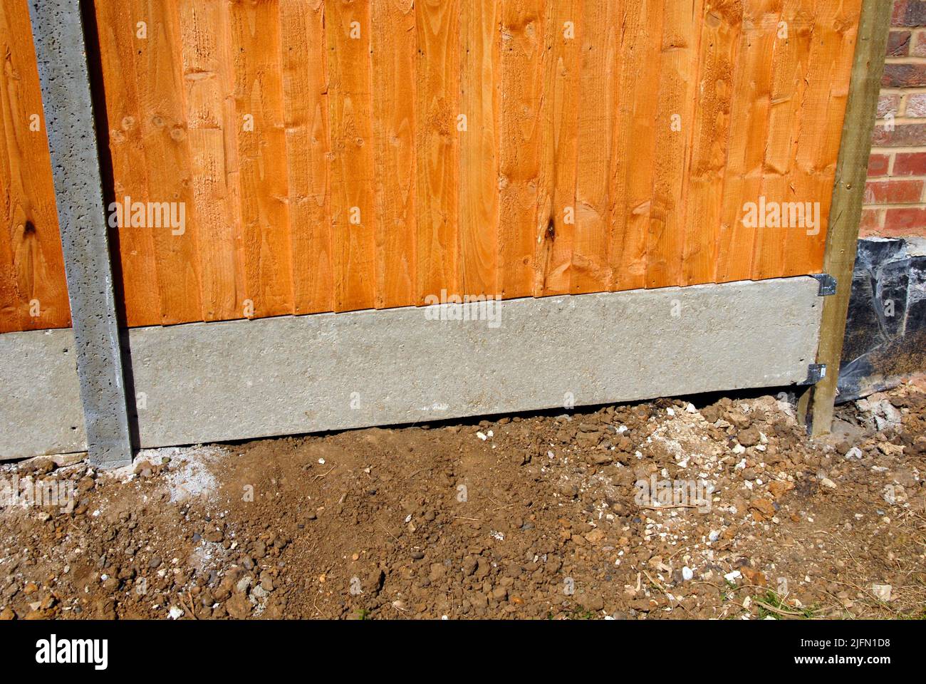 Fencing in area with undulating soil levels, using mix of concrete and wooden posts, wooden panel and concrete gravel board held up by metal brackets Stock Photo