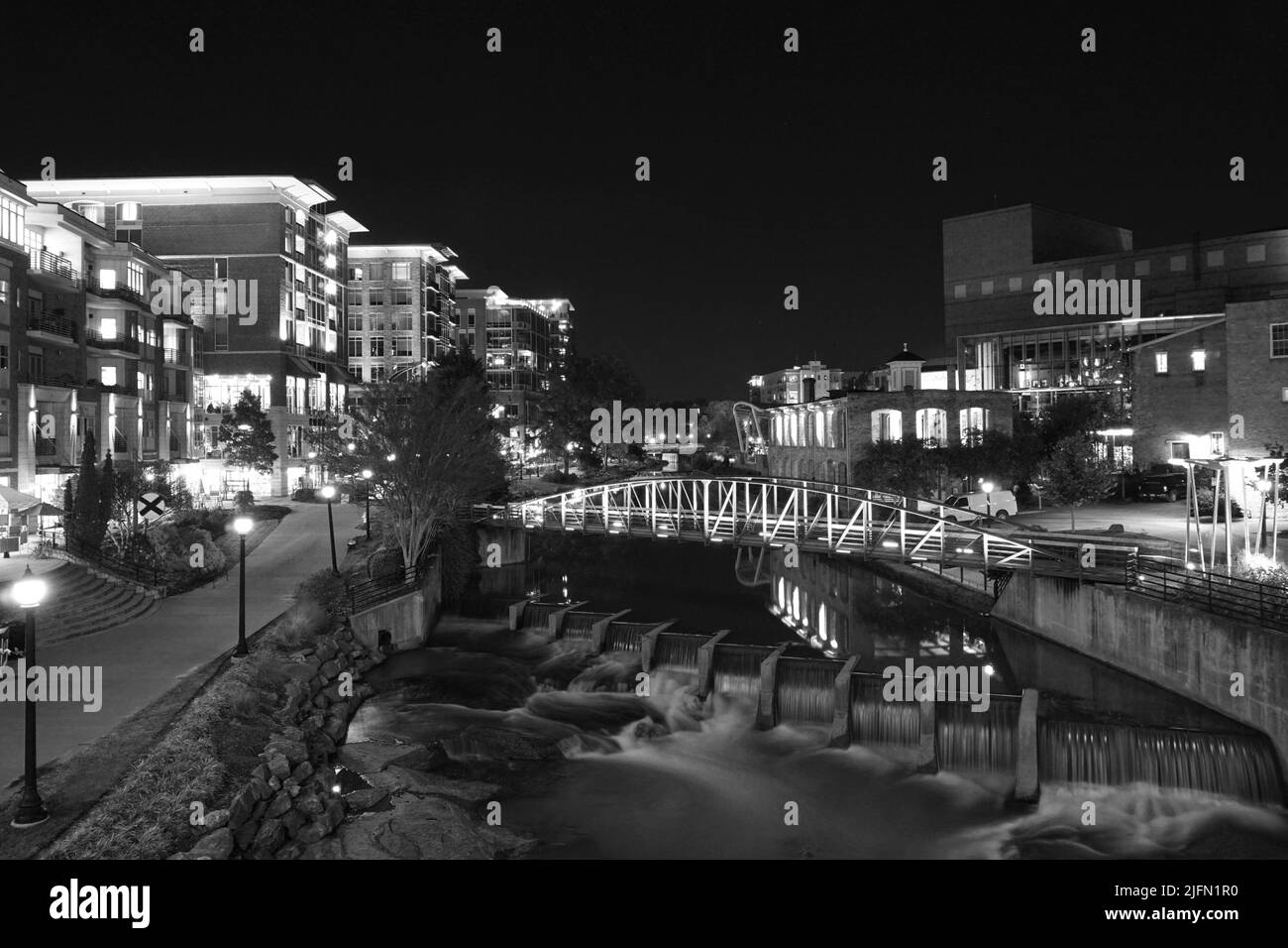 A night view of the Reedy River in downtown Greenville, SC USA. The lights of the buildings and bridge reflect in the water of the river. Shops and re Stock Photo