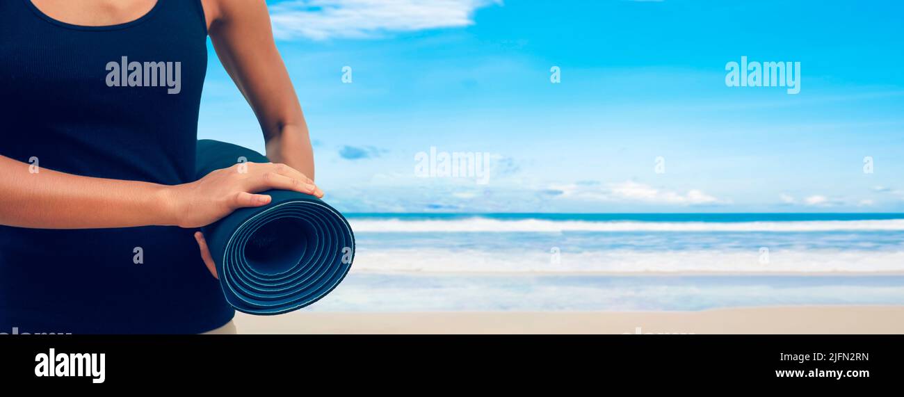 Woman in sport suite carry yoga mattress on the beach,Sport background.healthy lifestyle and travel. Sport female equipment Stock Photo
