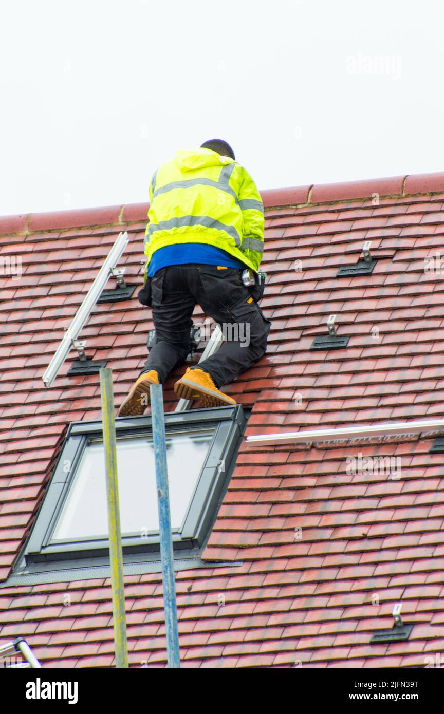 Workman working on slanted red tiled roof to install Solar panels Stock Photo