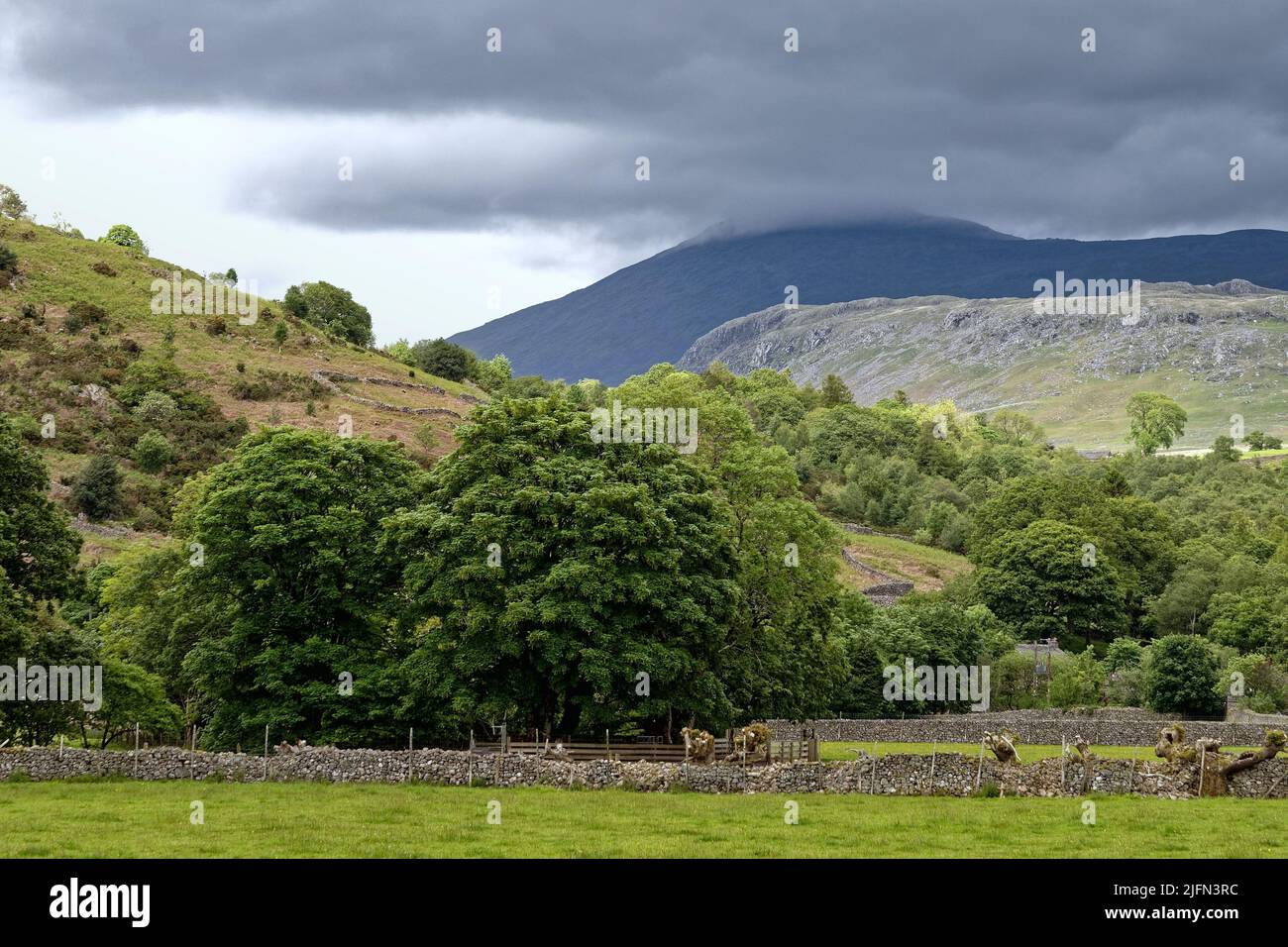 The Scafell range of mountains in storm clouds dominating the skyline in Boot, Eskdale on a summers day Lake District Cumbria England UK Stock Photo