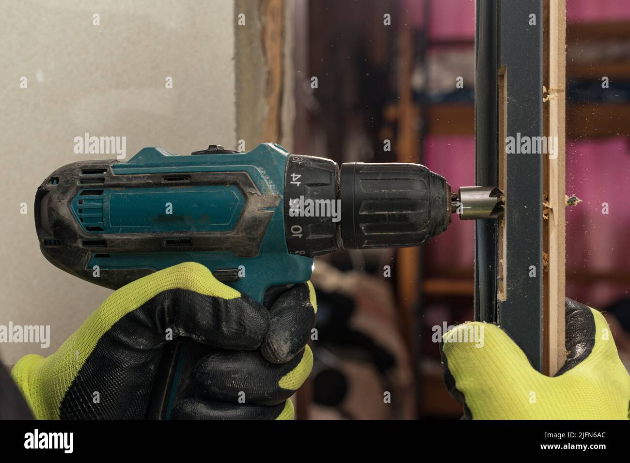 Drilling a hole in the door with a green screwdriver, closeup of the