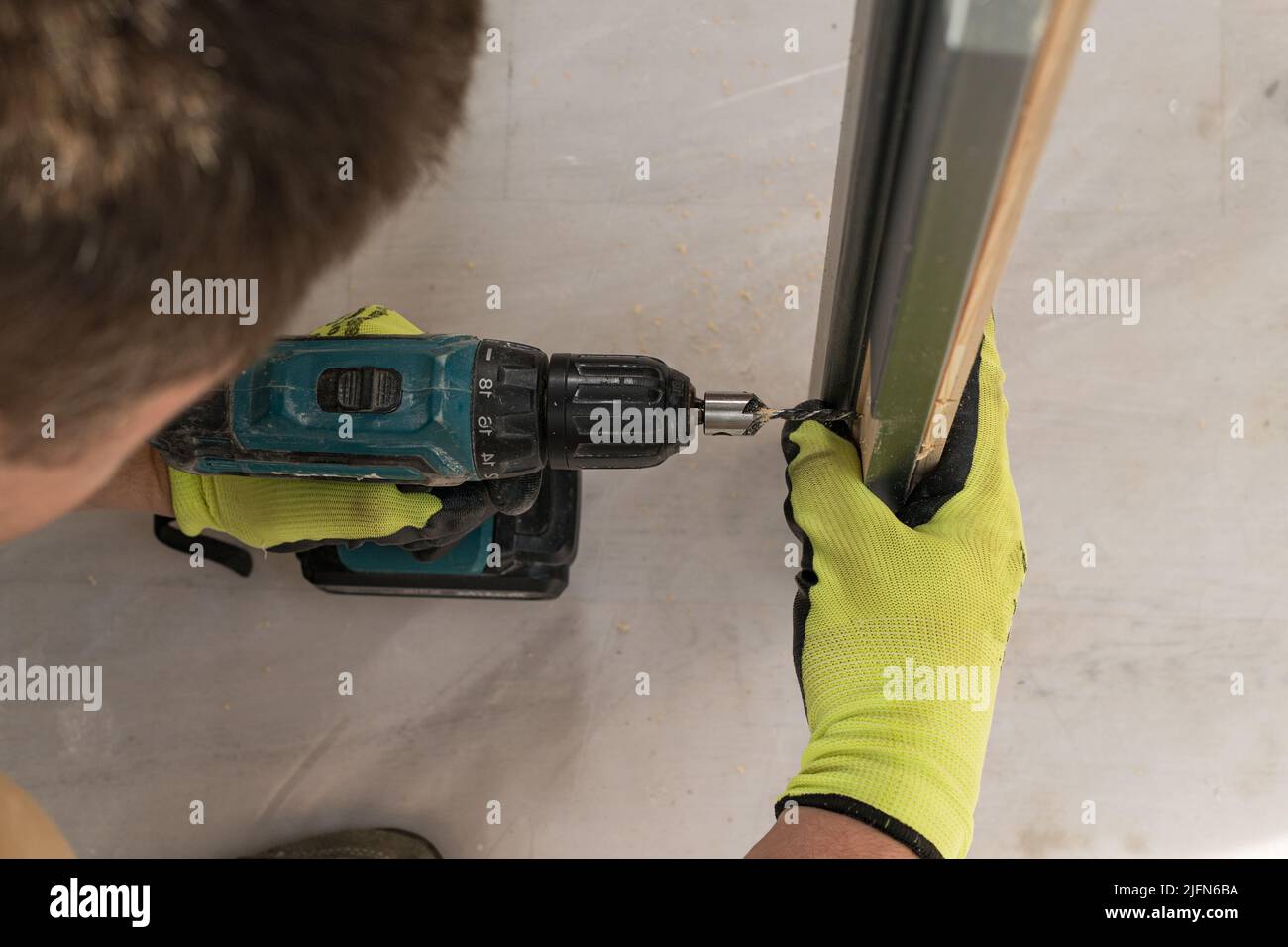 Drilling a hole in the door with a green screwdriver, closeup of the