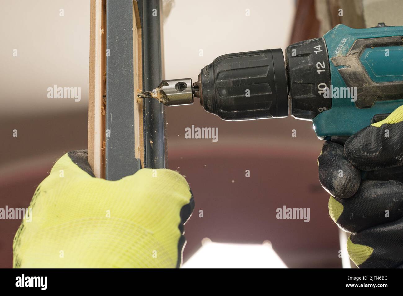 Drilling a hole in the door with a green screwdriver, closeup of the