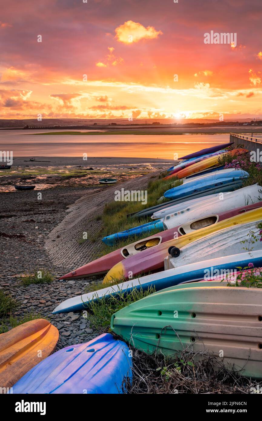 A row of canoes and kayaks make for a colourful foreground as the sun rises over the River Torridge estuary at Appledore in North Devon. Stock Photo