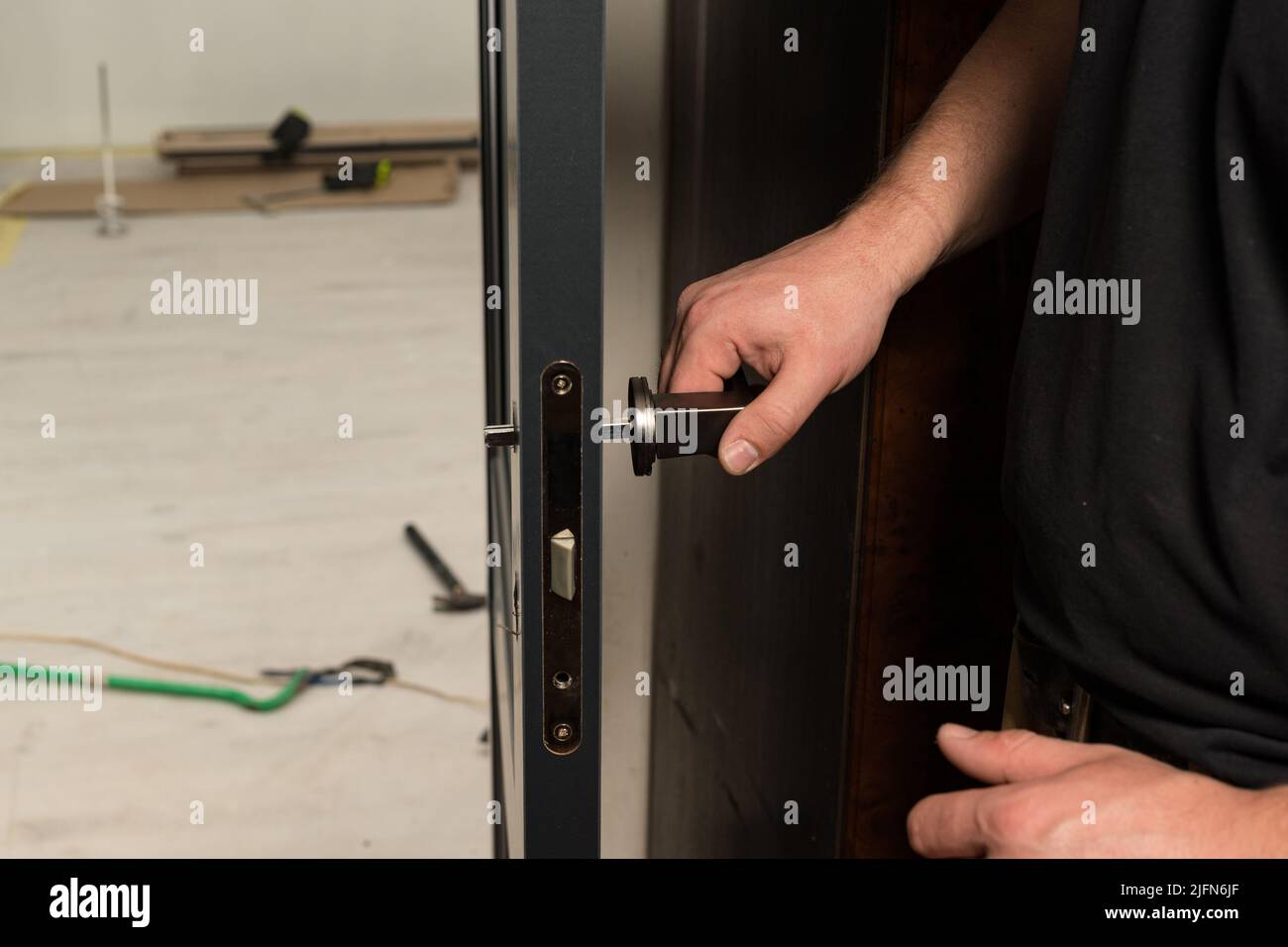 A carpenter installs a metal doorknob for an interior door, installing
