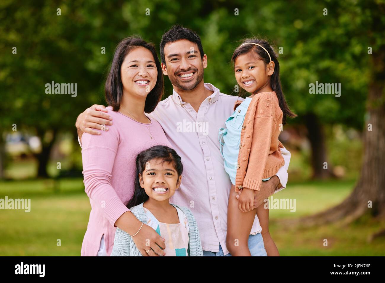 Portrait of happy asian family standing close together in a park. Adorable little girls enjoying free time with their mother and father on a weekend Stock Photo