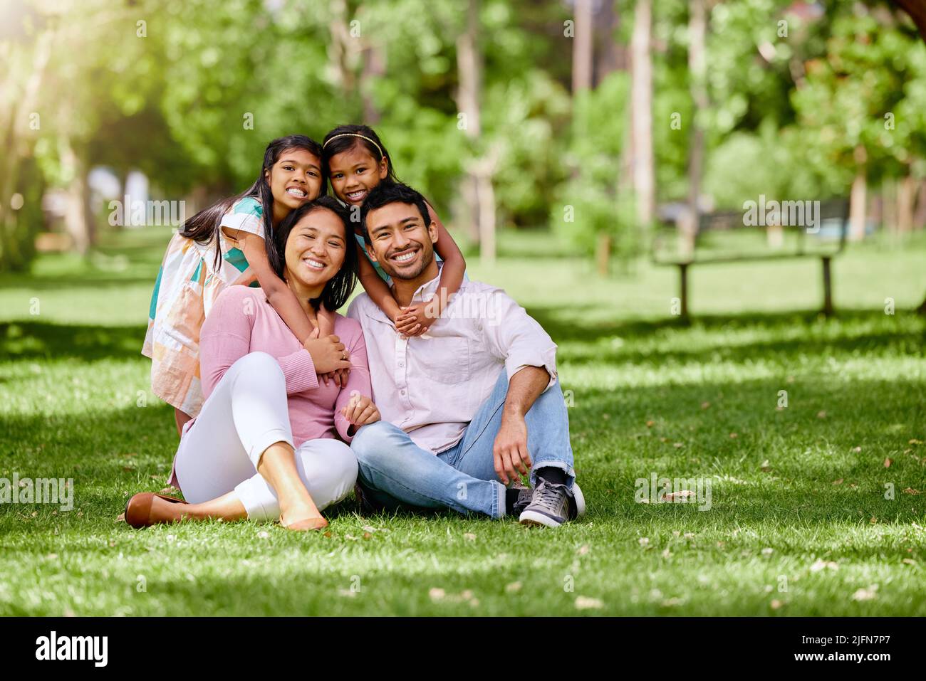 Portrait of happy asian family in the park. Adorable little girls bonding and hugging their parents outside in a park. Full length husband and wife Stock Photo