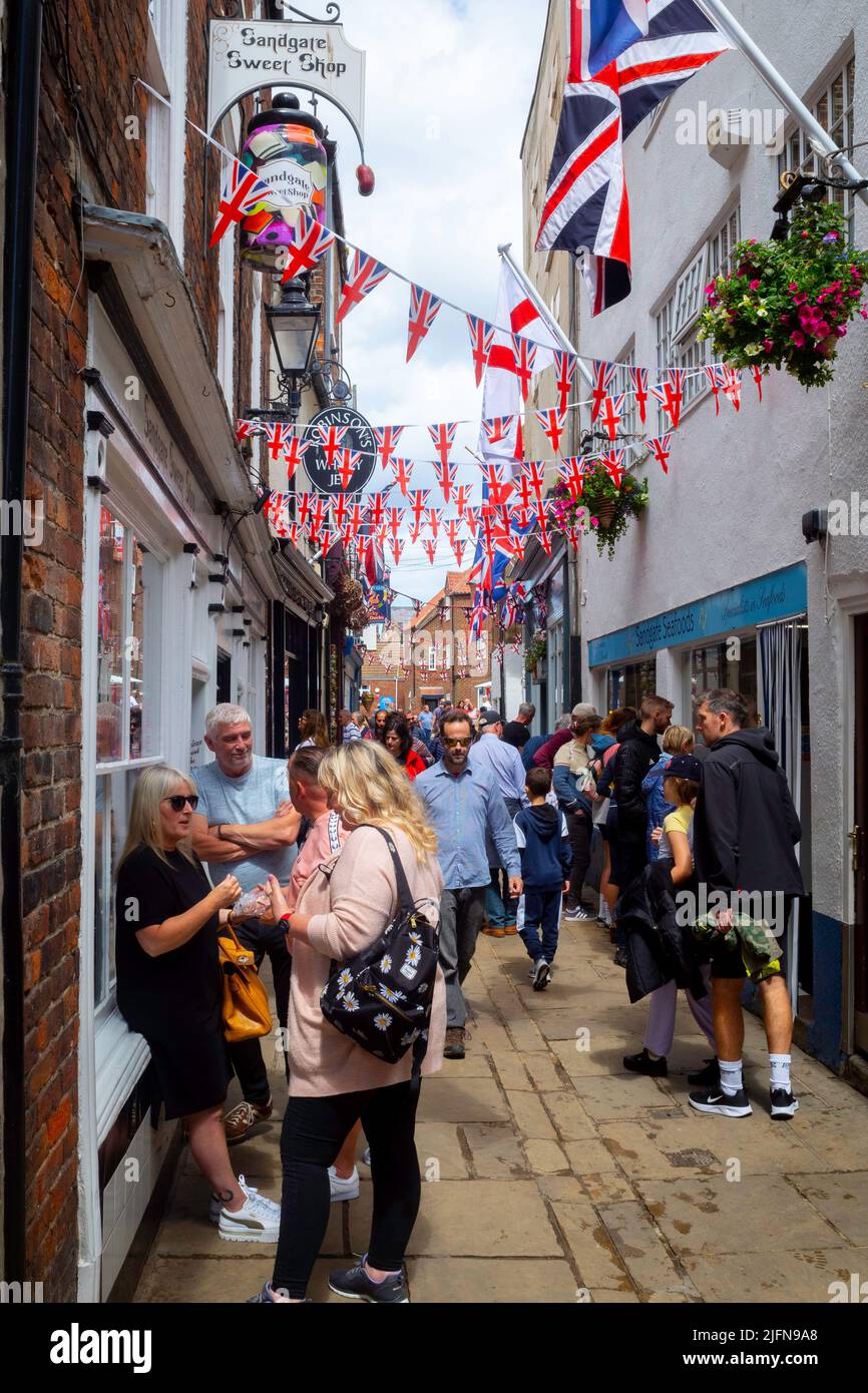 A warm summer's day on Sandgate Whitby decorated with union flags with people shopping for holiday goods Stock Photo