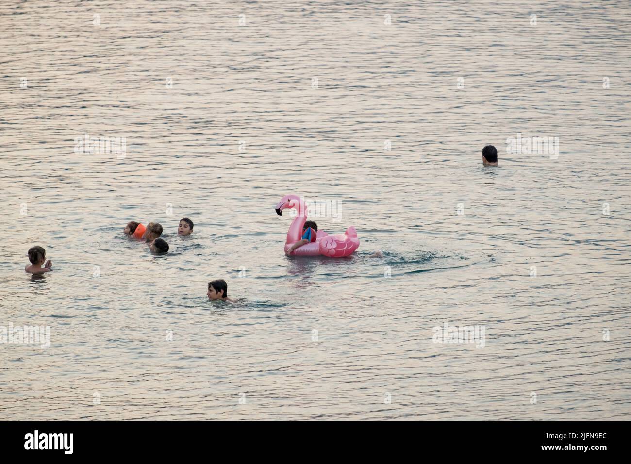 Kids swimming and playing with inflatable flamingo in the calm waters of the Aegean sea Stock Photo