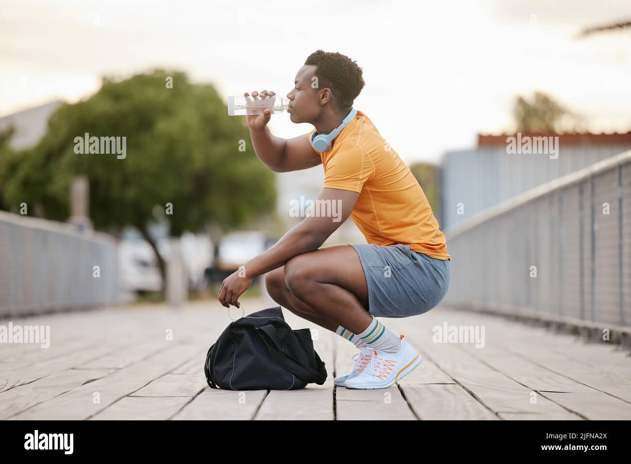 An African American man drinking water on a bridge. A man taking a break from exercising drinking from a bottle. A sporty guy focusing on health. Stock Photo