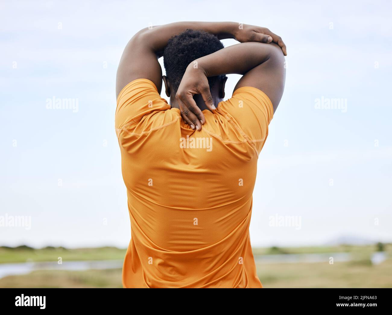 Rearview of a runner stretching on a field. An African American man focused on warming up. A sportsman staring forward away from the camera Stock Photo