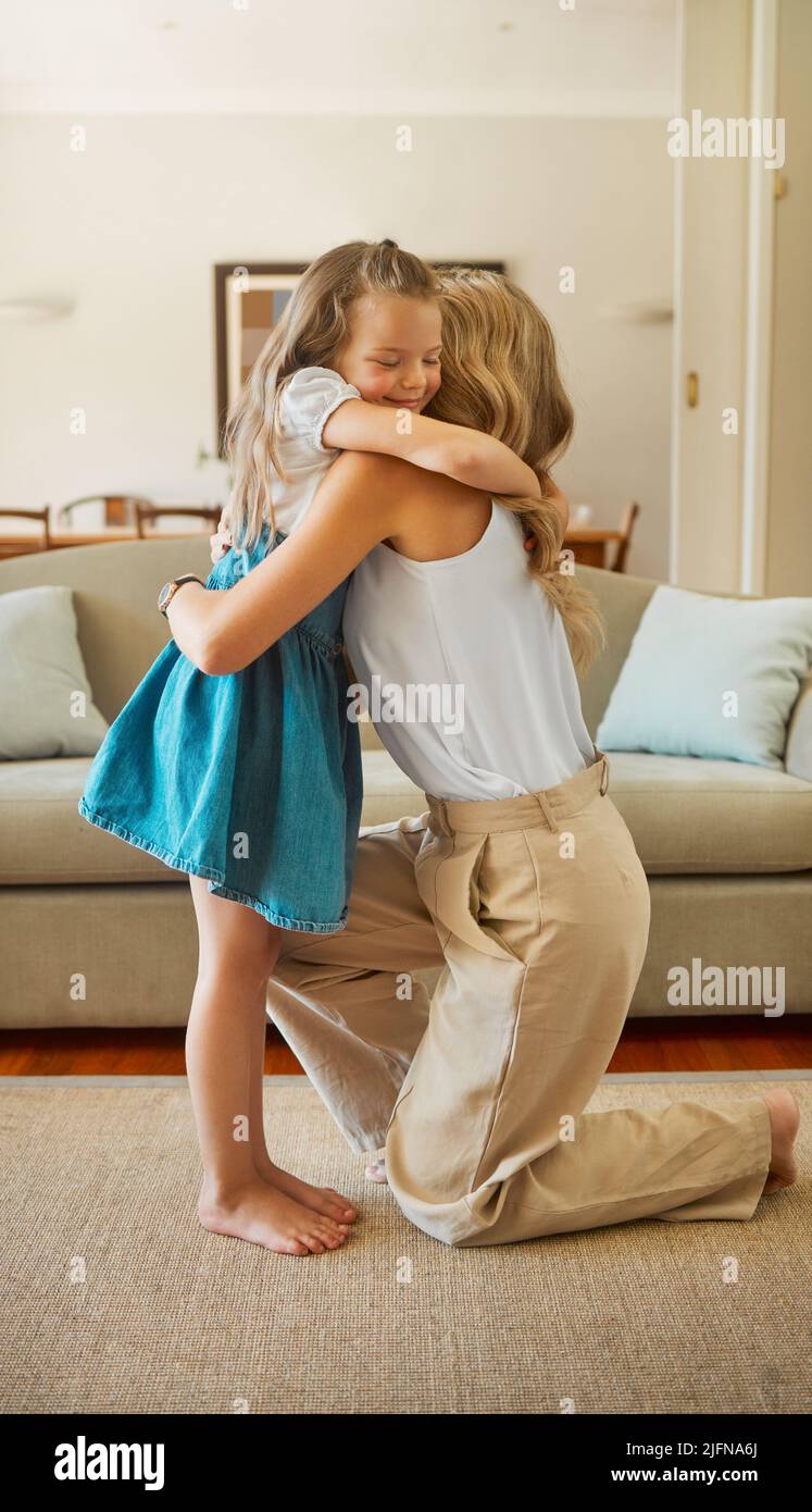 Young content mother and daughter hugging each other in the lounge together at home. Mom embracing her happy little girl standing at home. Child Stock Photo