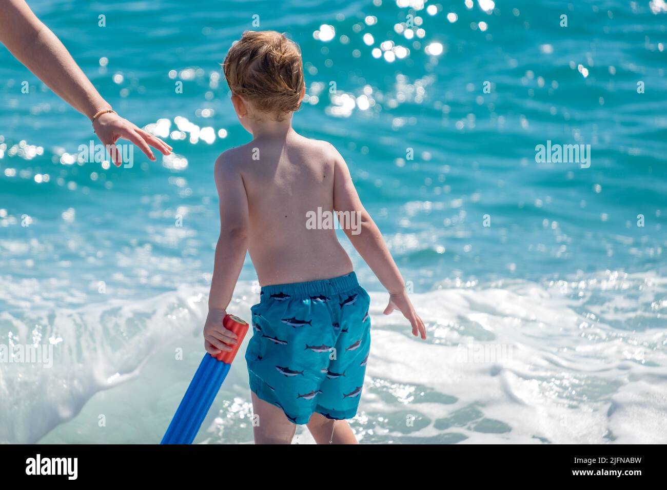 Cute little boy with blond hair playing with his water gun in the beach Stock Photo