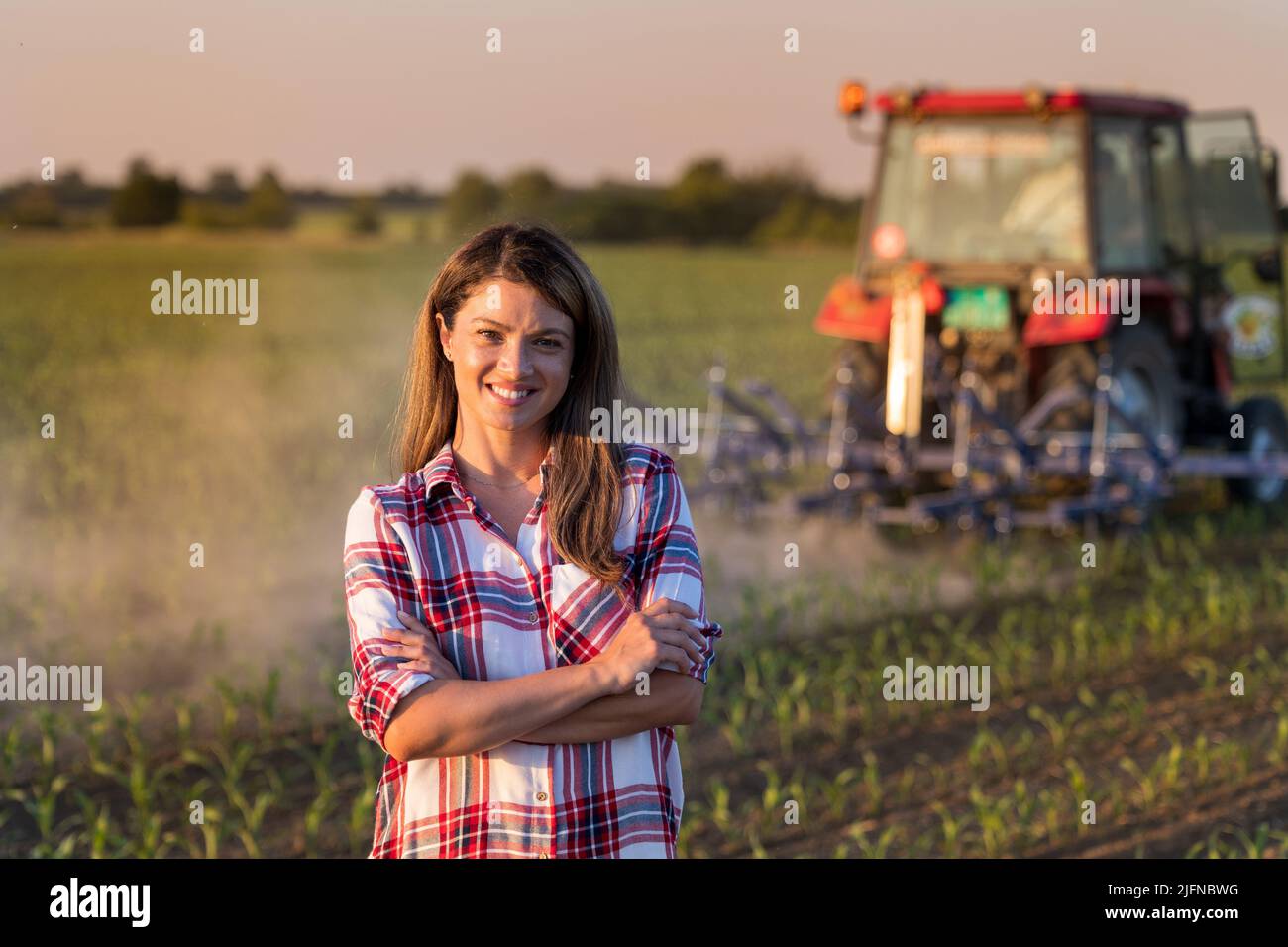 Portrait of pretty young farmer woman standing with crossed arms in ...
