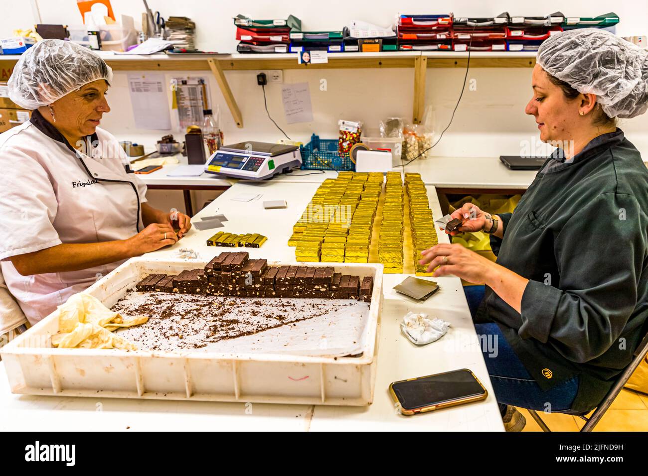 In the cool morning, the bestseller of the chocolate manufactory Frigoulette is wrapped by hand in golden paper. Malakoff chocolates, nut nougat chocolates with 68% cocoa content and roasted hazelnuts. During the summer, production is underway for Christmas. Frigoulette supplies stores throughout France with Malakoff chocolates Stock Photo