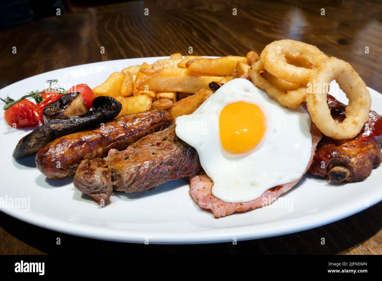 A traditional English mixed grill. A British pub meal classic. The plate contains four different grilled meats, a fried egg, chips, fried onion rings Stock Photo