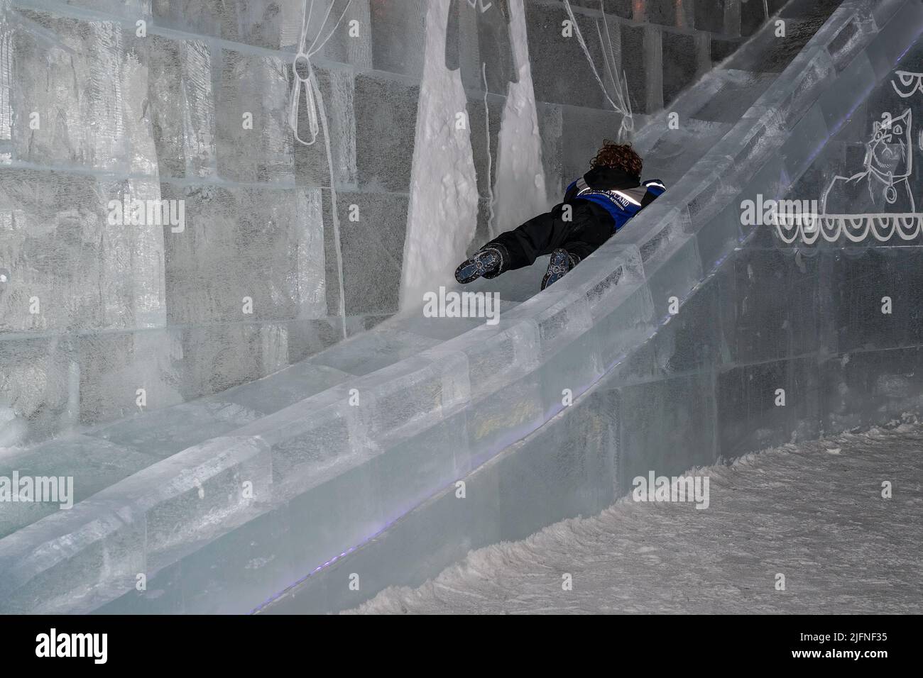 Kemi, Finland - March 21st, 2022: A boy sliding backwards on a slide carved of ice, in the Lumilinna snow castle in Kemi, Finland. Stock Photo