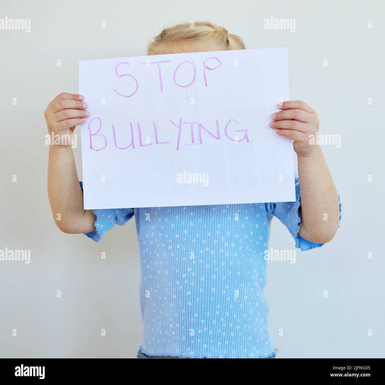 Little girl holding a paper with message that bullying at school must be stopped. Blonde child actively protest against bullying, kid starting an anti Stock Photo
