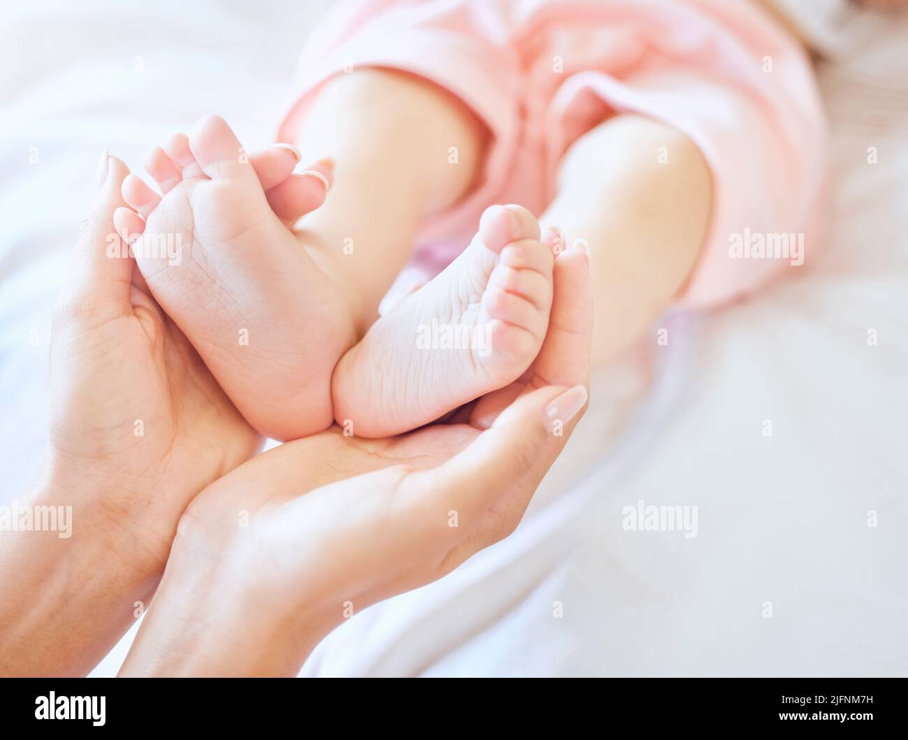Mother holding baby feet. Closeup of tiny newborn baby feet held by a parent. Small baby toes. Little baby lying on a bed. Woman holding feet of Stock Photo