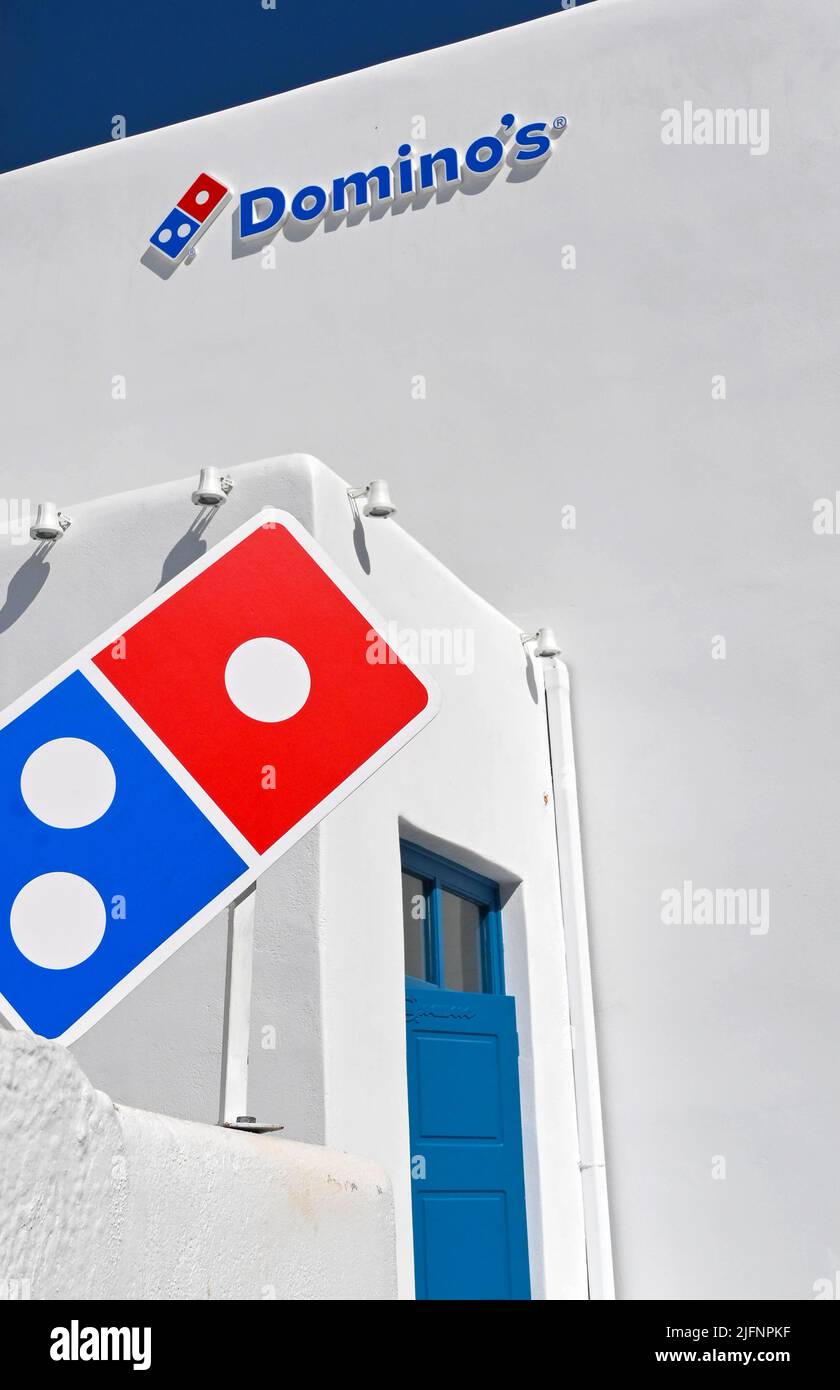 Mykonos, Greece - June 2022: Sign on the outside of a Domino's pizza outlet. The building is covered in traditional whitewash. Stock Photo
