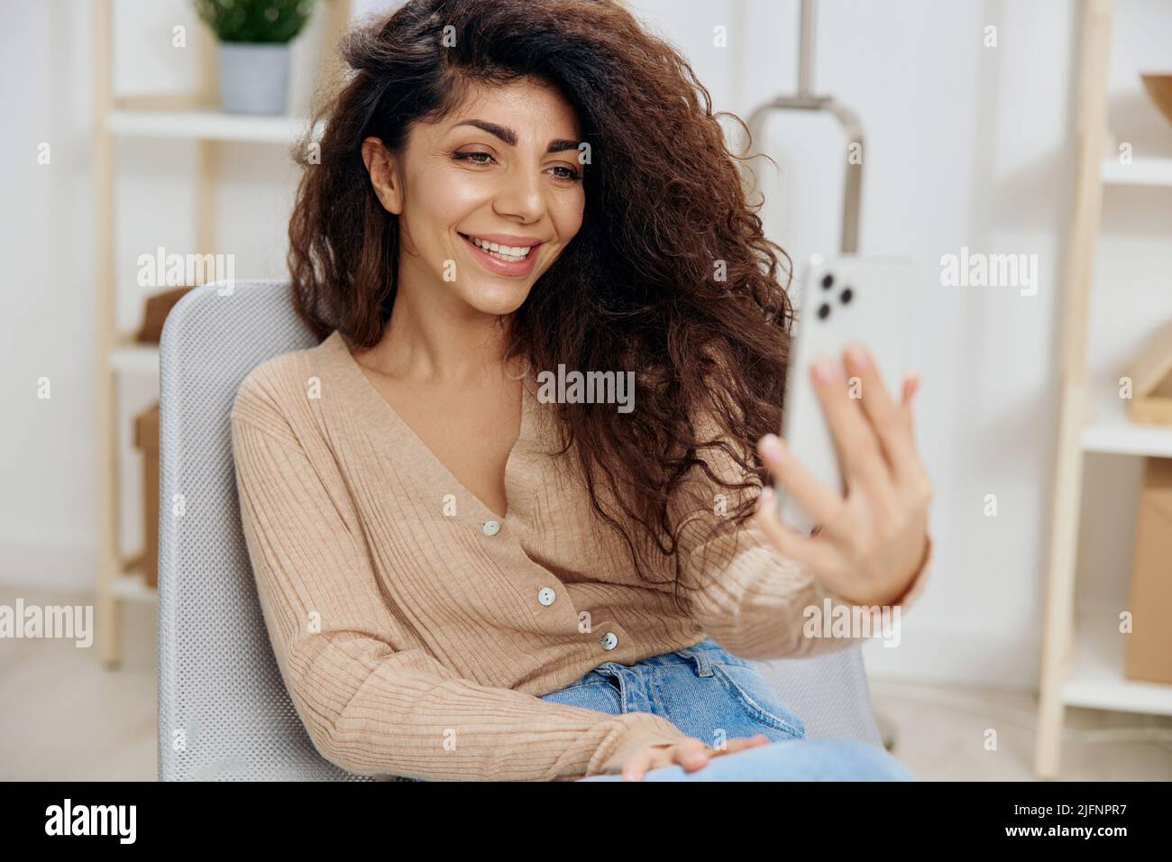 Smiling happy cute tanned curly Latin lady doing selfie video call with