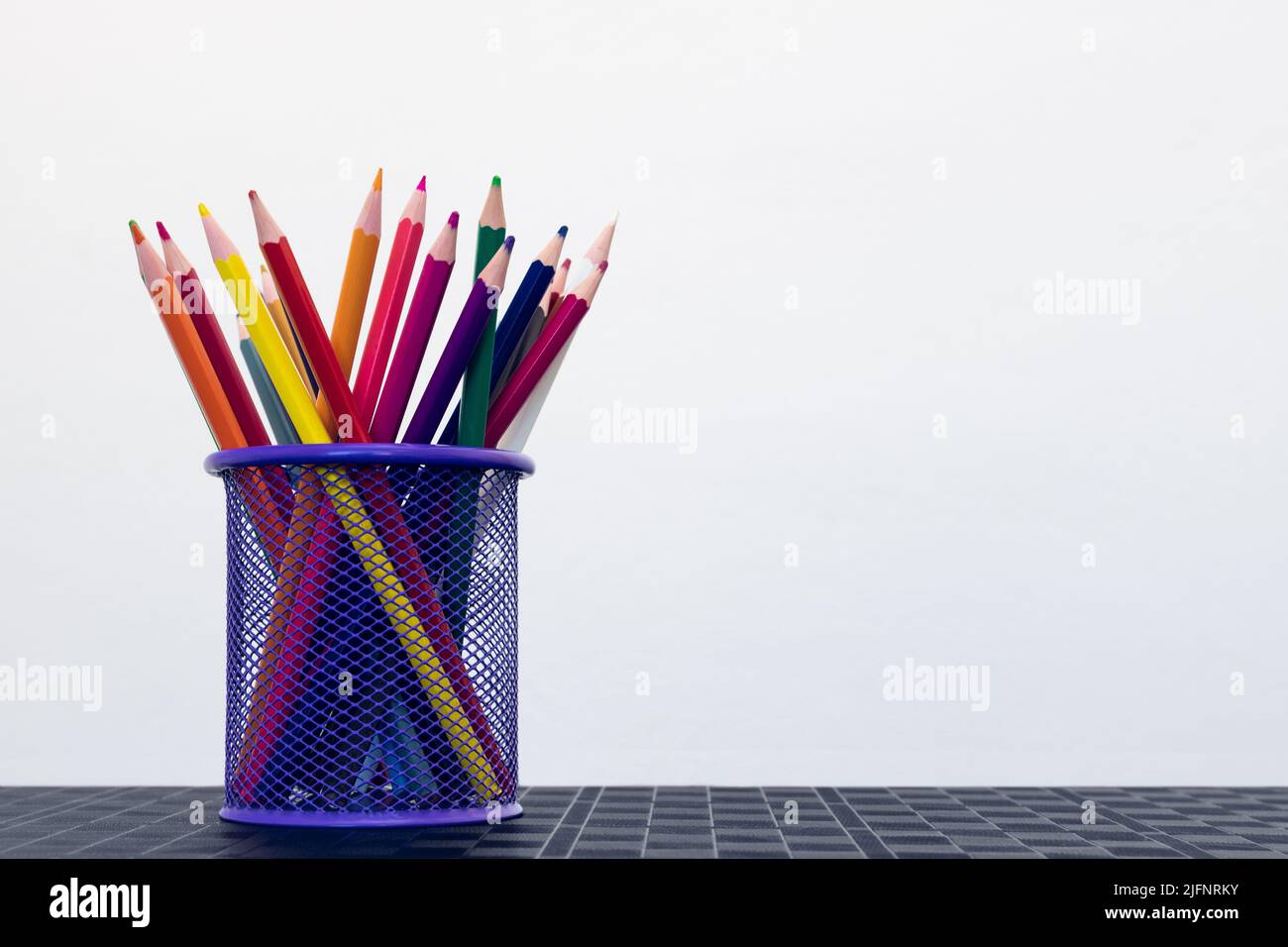 Colored pencils in a pencil holder on the office desk isolated on a white background. Empty space for text Stock Photo