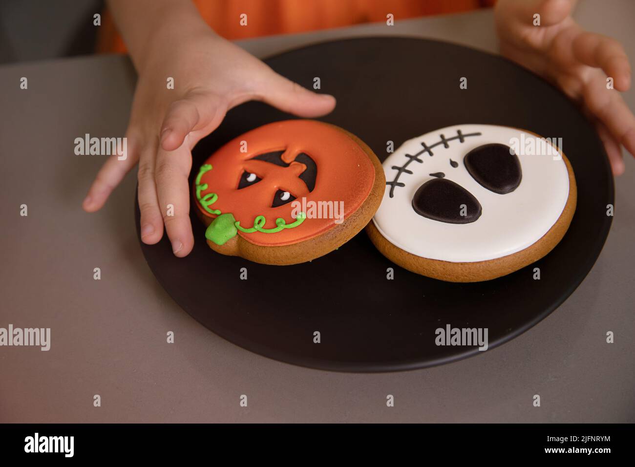 Girl's hand reaches for homemade Halloween cookies with painted faces Stock Photo