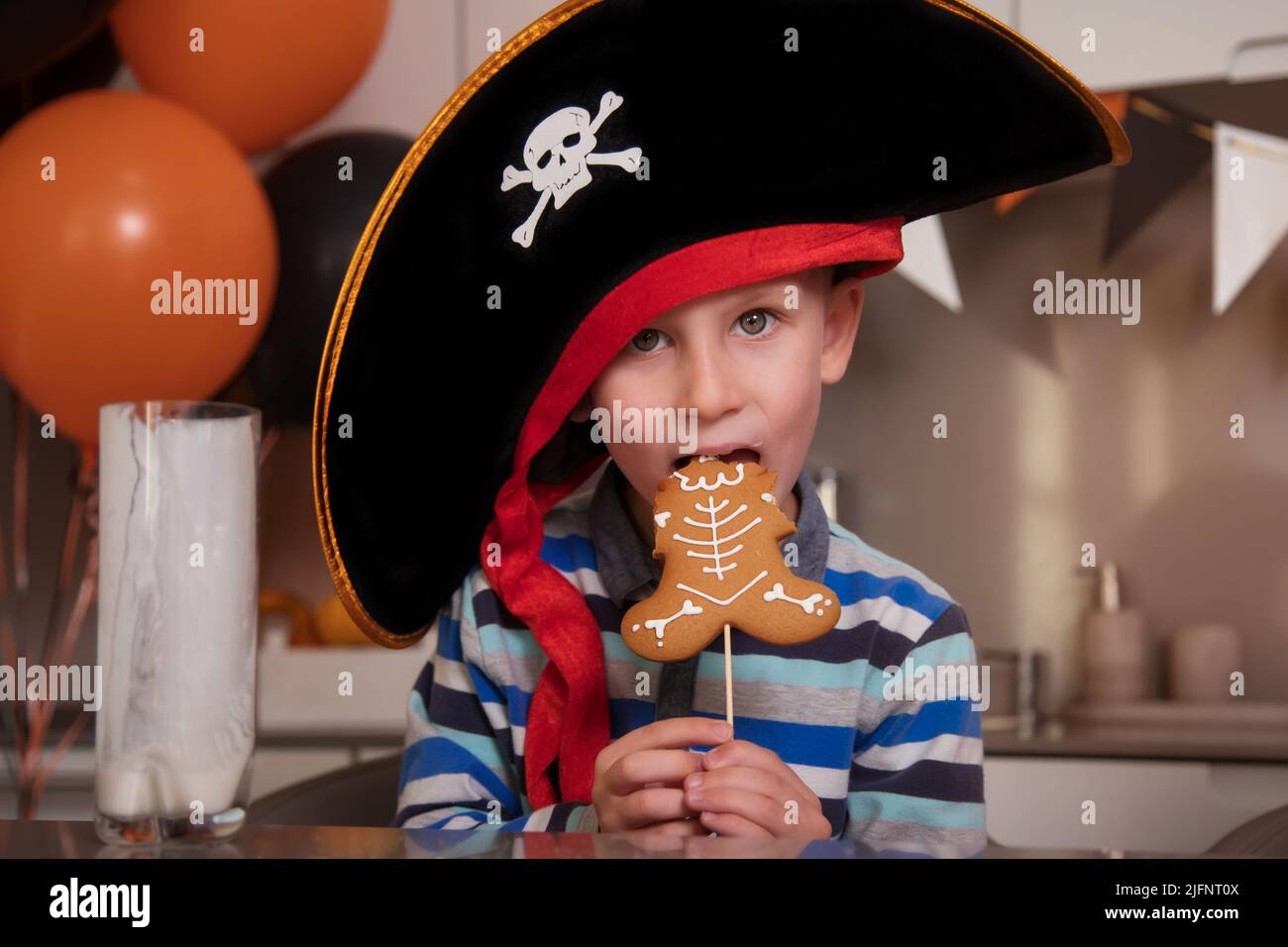 A boy dressed as a pirate eats gingerbread as a Halloween skeleton, drinks milk Stock Photo