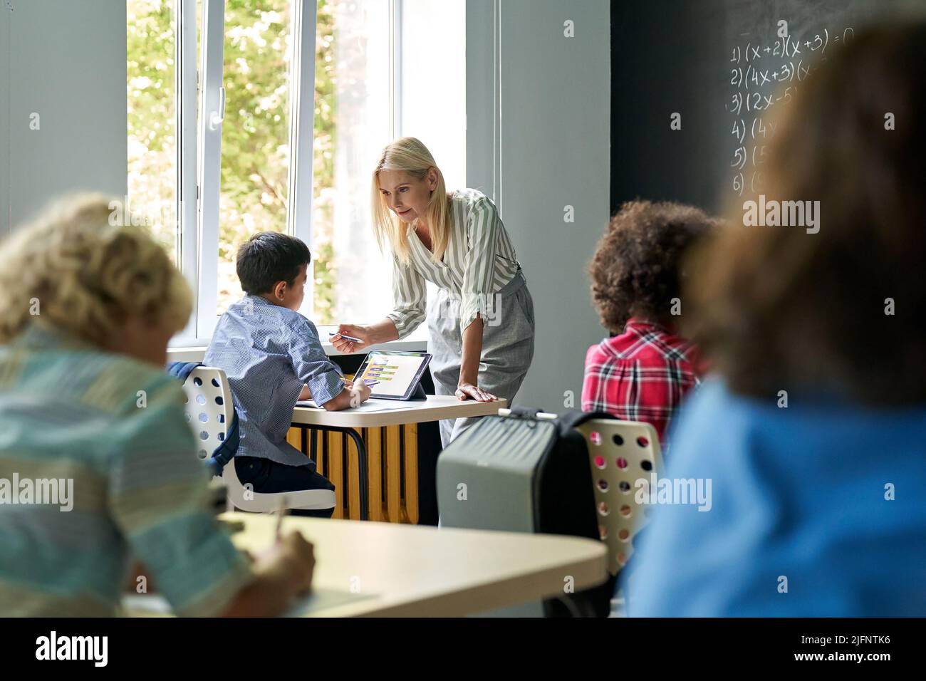 Happy blonde teacher explaining maths at lesson to student. Education concept. Stock Photo