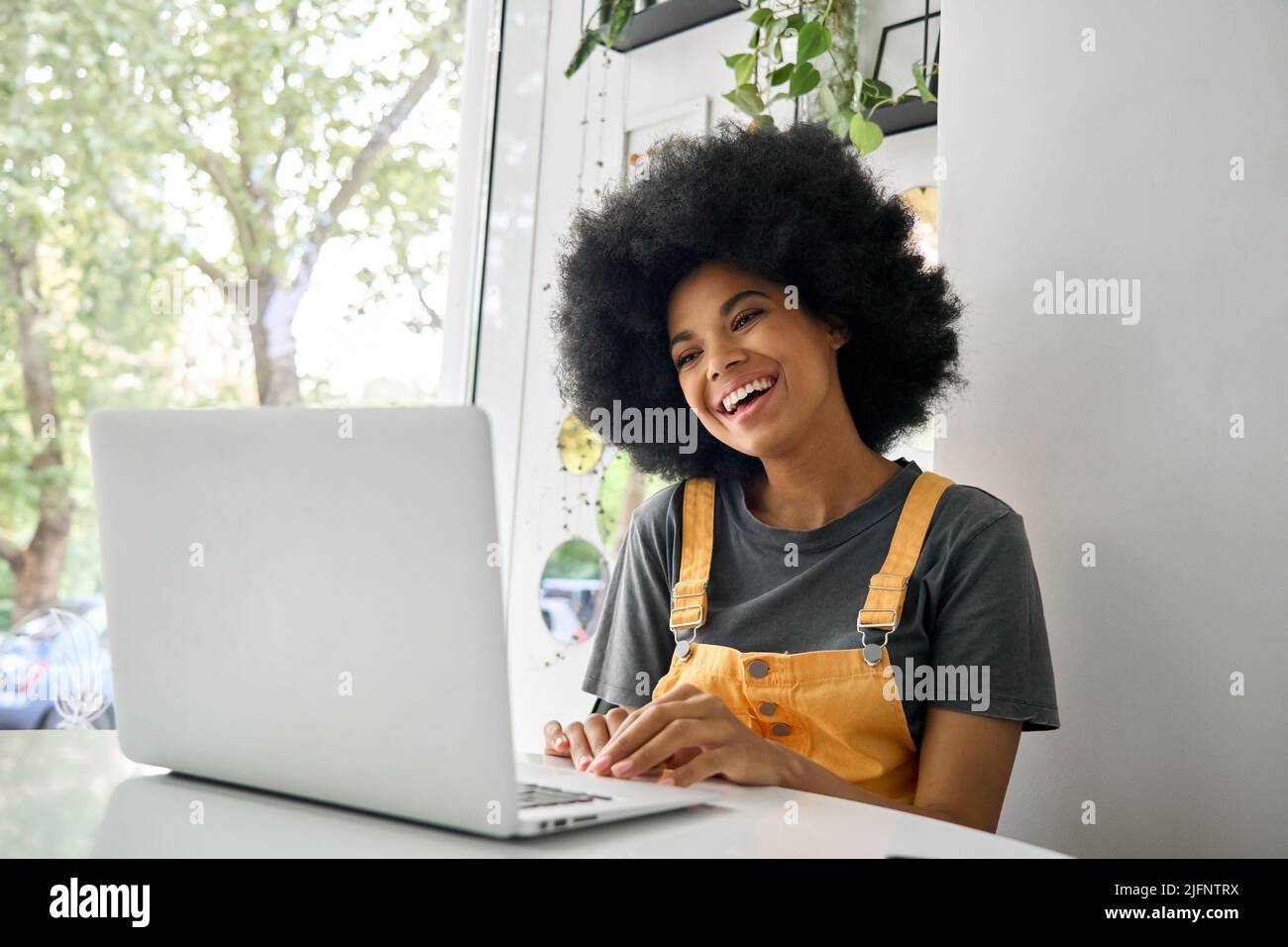 Smiling young woman sitting in cafe having video call using laptop. Stock Photo