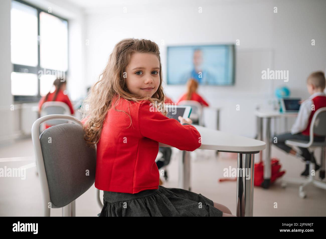 Happy schoolgirl wearing school uniform sitting in class and smiling in ...