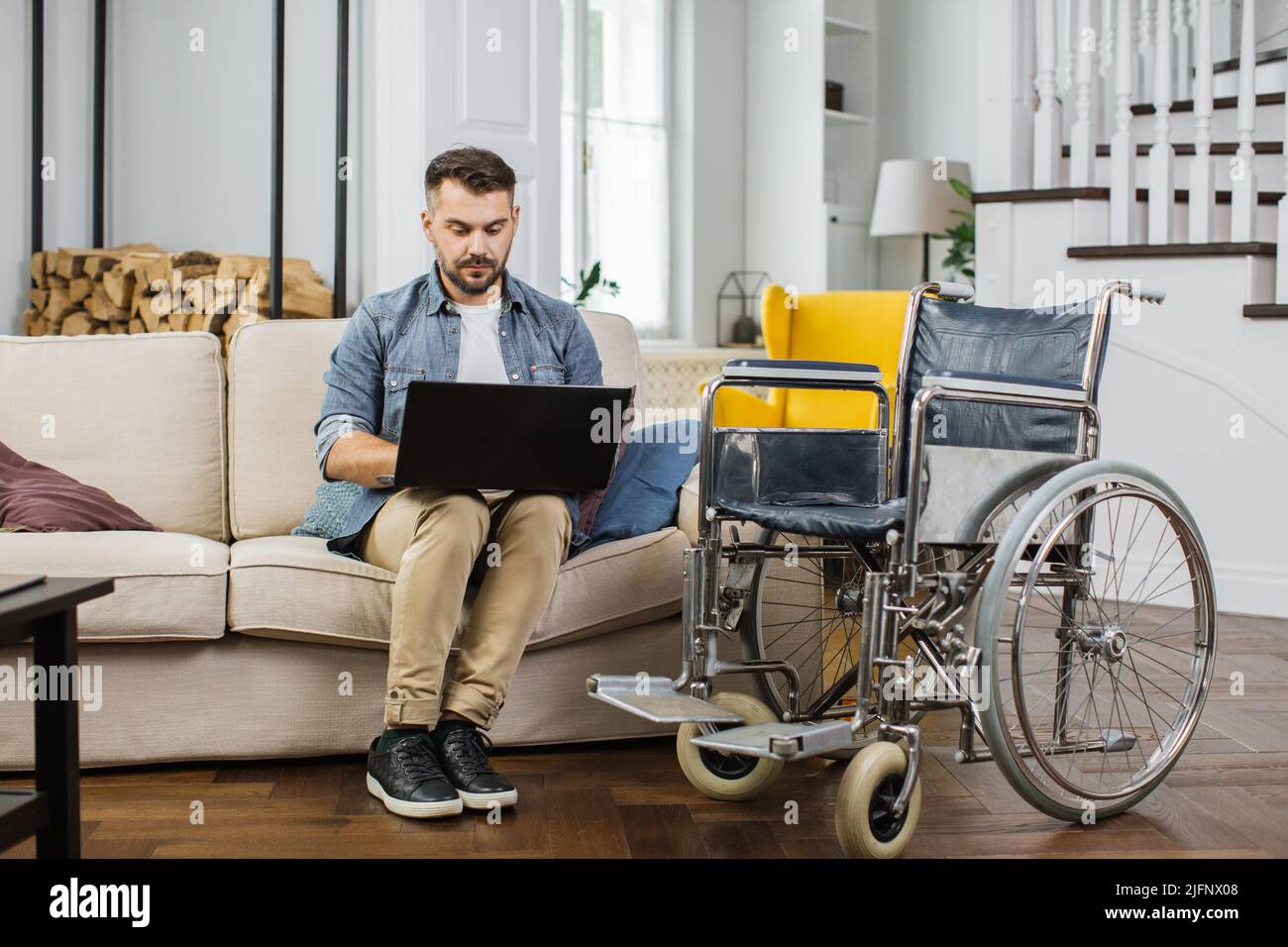 Motivated male freelancer with special needs sitting on comfy sofa near  wheelchair and typing on laptop at home. Concept of distant work and people  with disability Stock Photo - Alamy