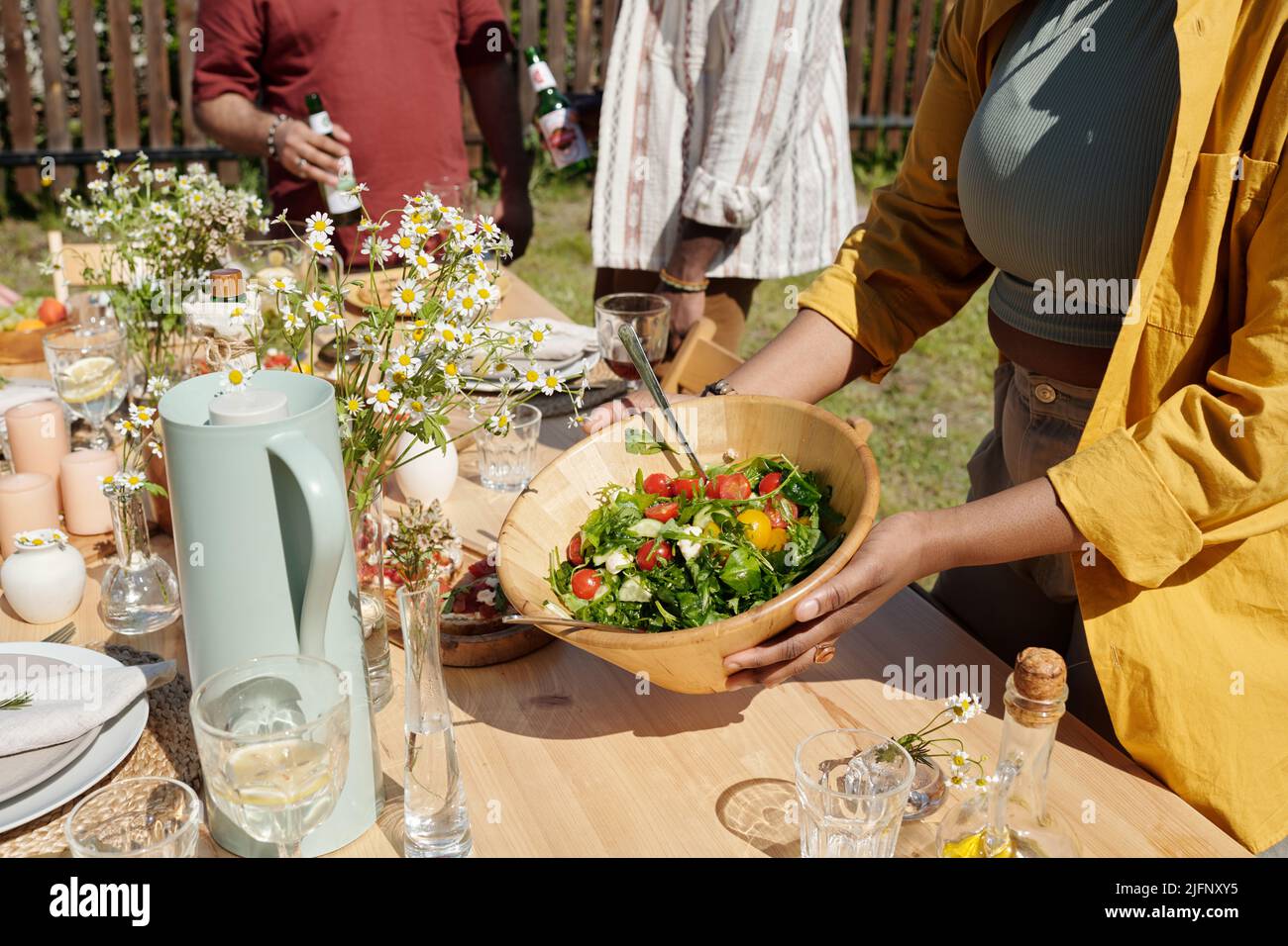 Young black woman serving table with homemade food, drinks, wildflowers