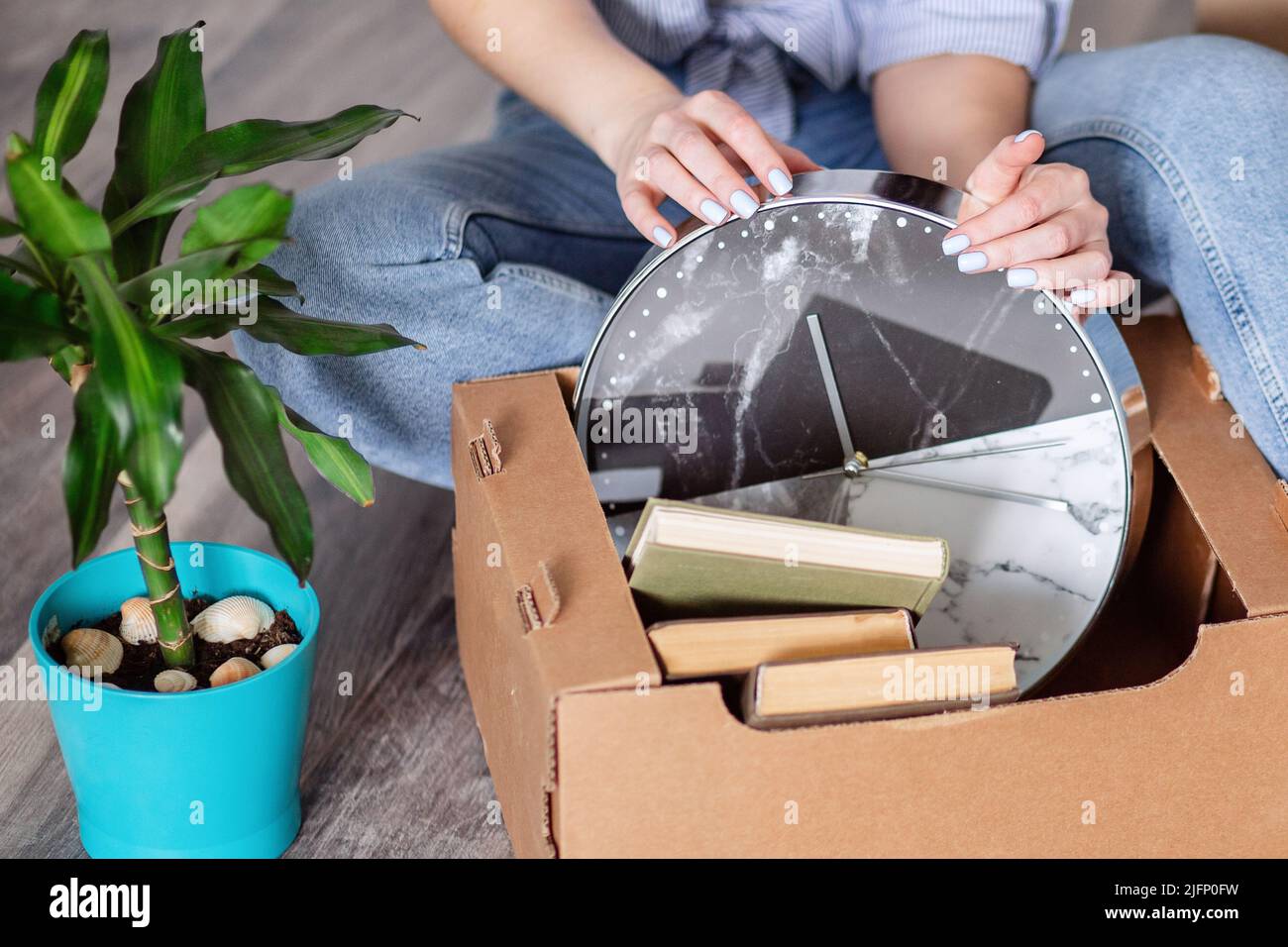 A woman takes things out of a cardboard box after moving. Hands takes out watches, books. Cleaning of things and order in the house. Stock Photo
