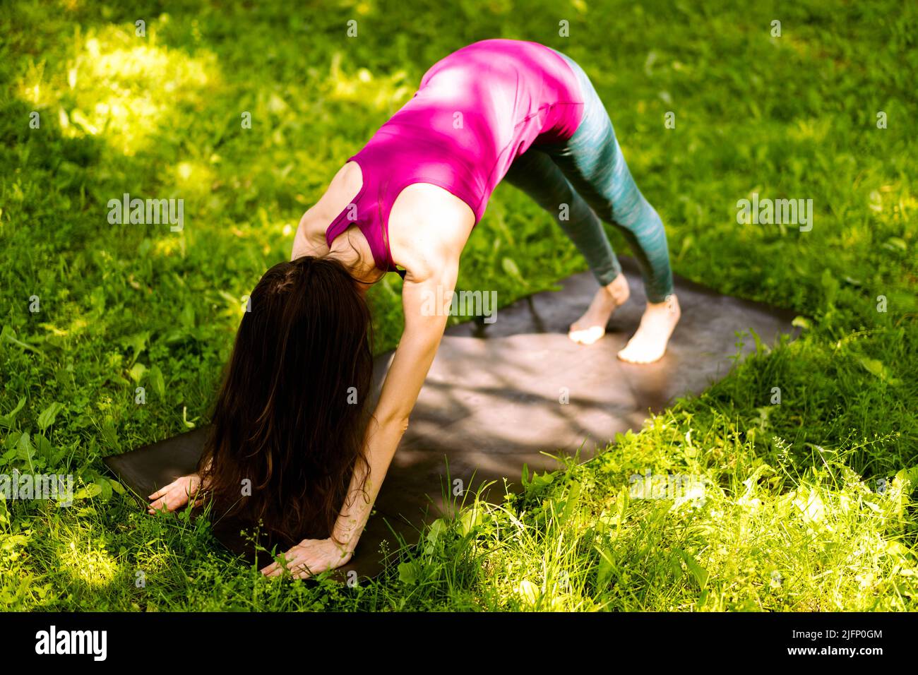 Beautiful young woman practices yoga asana eka pada Adho Mukha Shvanasana. The girl is dressed in a sporty red top and leggings.  Stock Photo