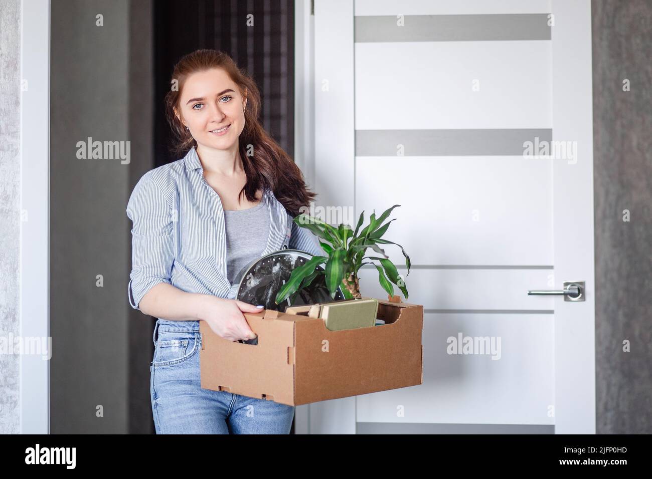 A young brunette woman is happy with the housewarming. A girl holds a cardboard box with things moving to a new apartment at a new place of work.  Stock Photo