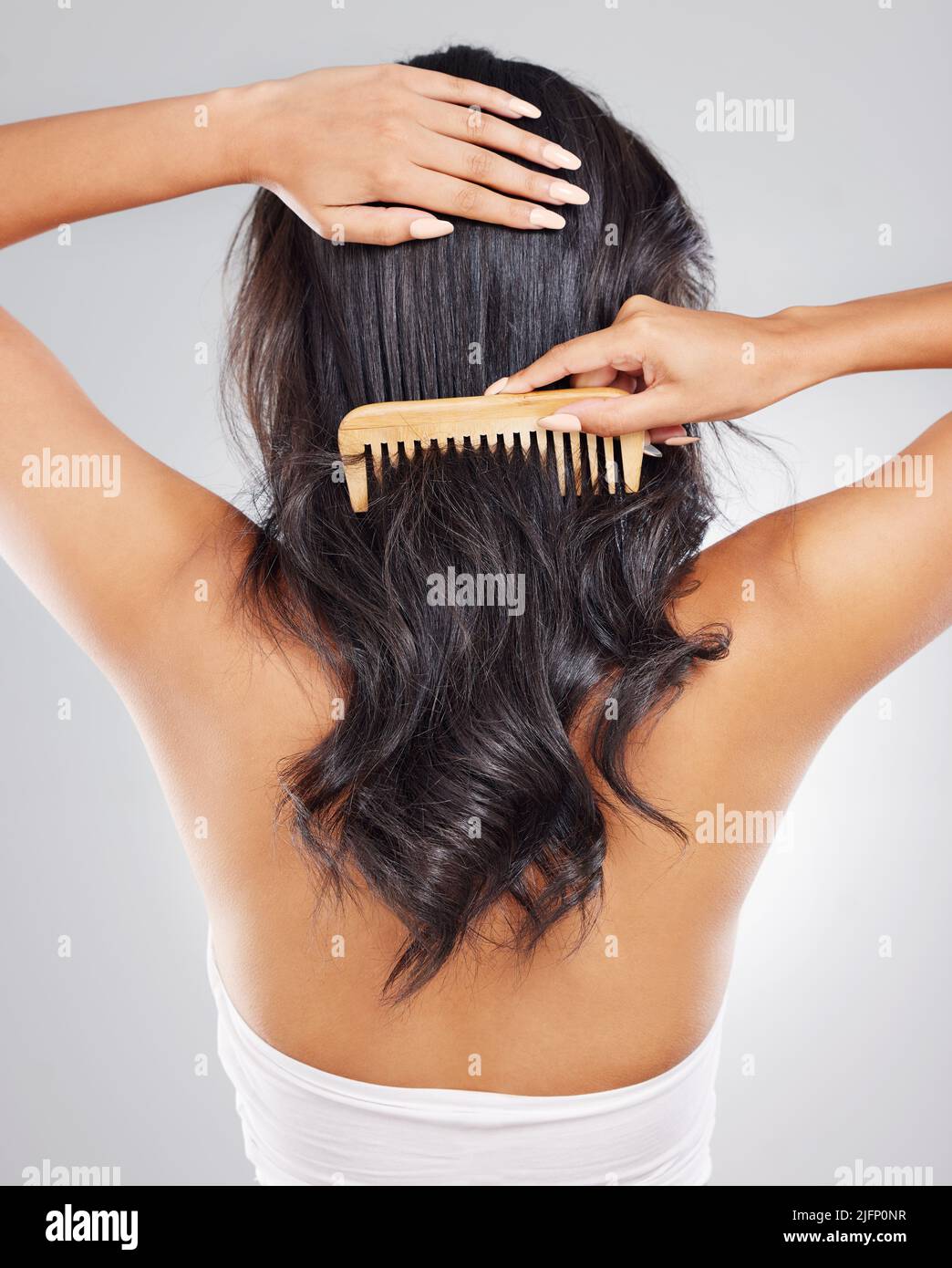 No knots allowed. Rearview shot of an unrecognizable young woman combing her hair against a grey background. Stock Photo
