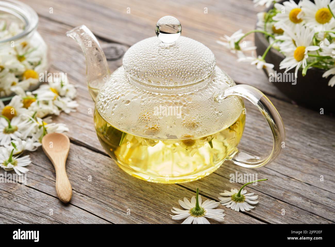 Glass tea kettle of healthy chamomile herbal tea. Chamomile daisy flowers on wooden table. Alternative herbal medicine. Stock Photo