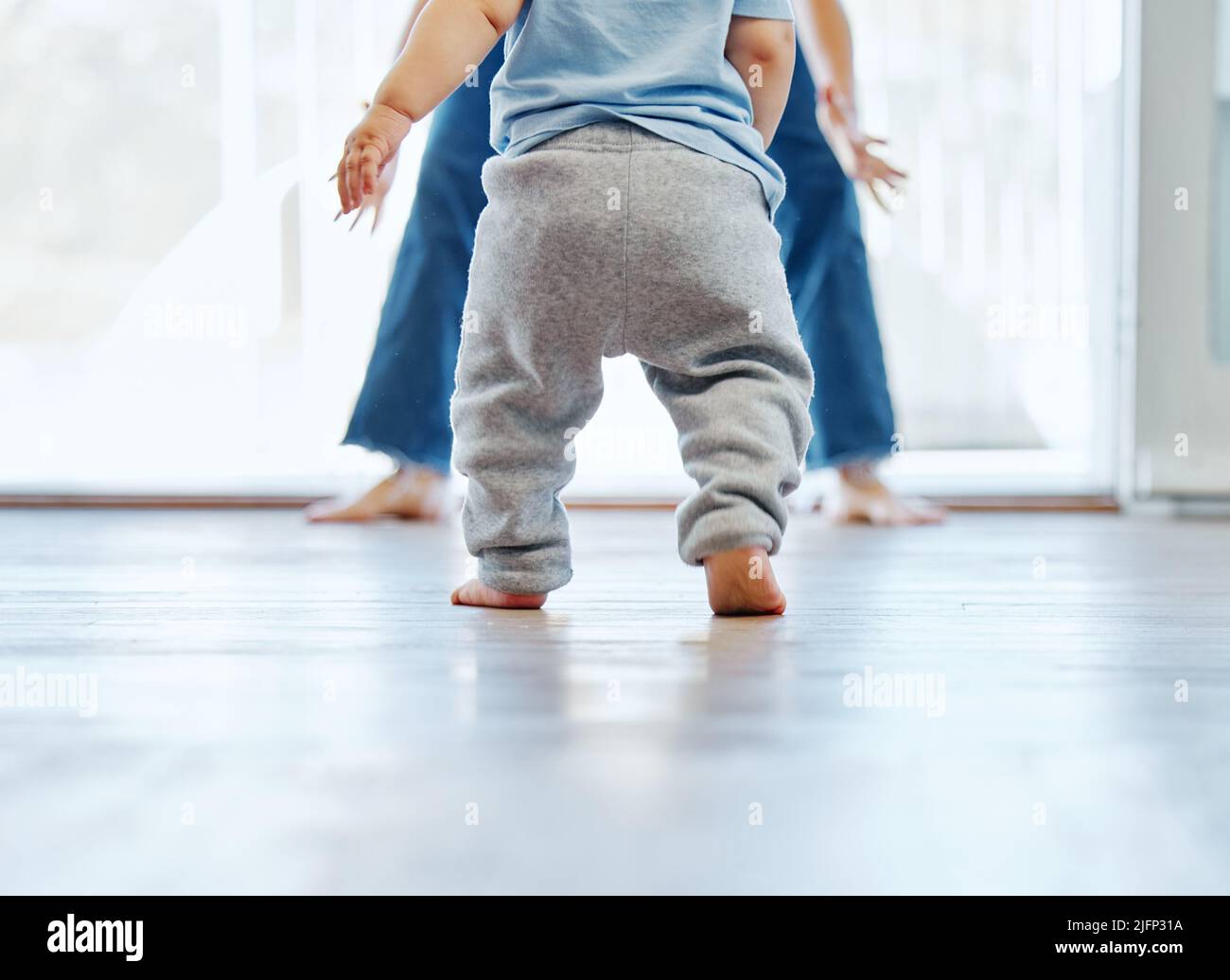 Taking his first steps on his own. Cropped shot of an unrecognizable little boy learning to walk with the help of his mother at home. Stock Photo