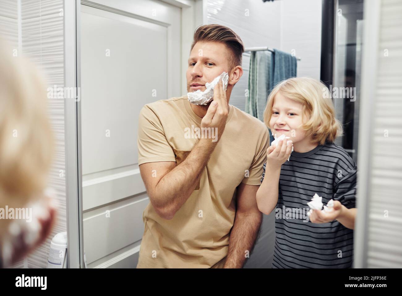 Portrait of father and son shaving together looking in mirror during morning routine in bathroom Stock Photo