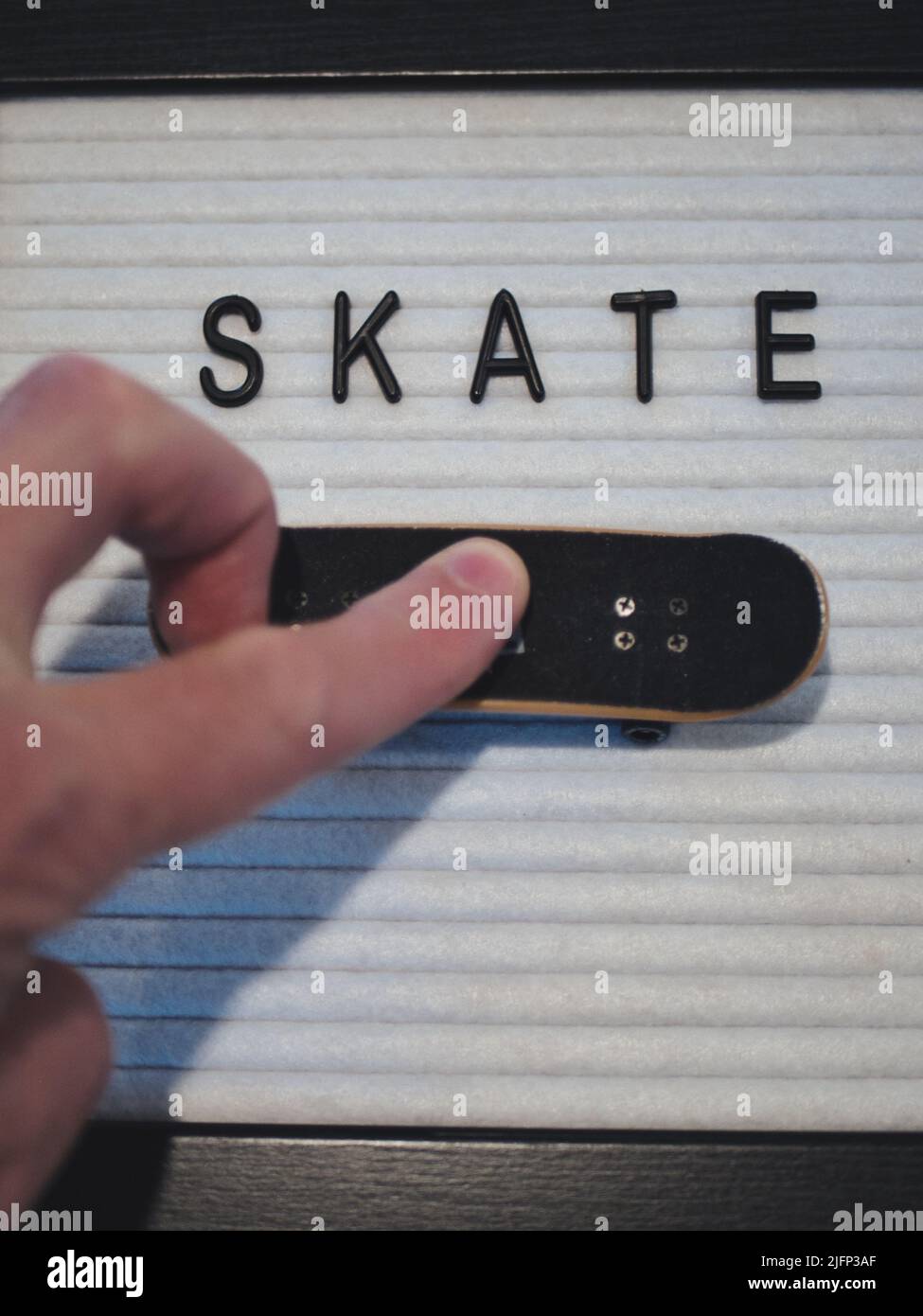 Skate in black text. Professional fingerboard expert about to do a 360 kickflip (tre flip). Fun graphic to illustrate skateboarding in a royalty free Stock Photo