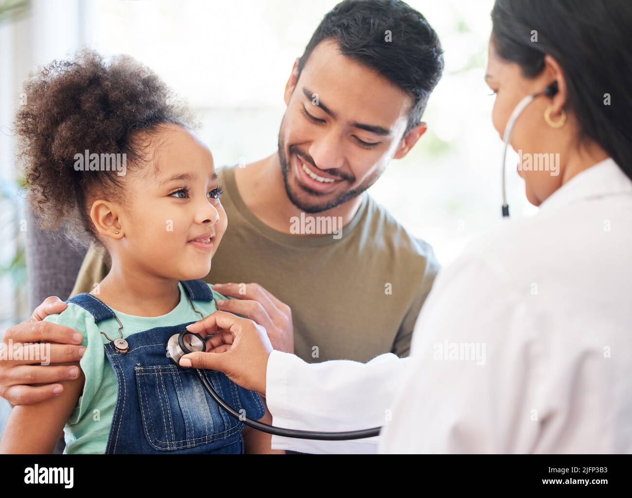 Shes very healthy, dad. Shot of a little girl sitting on her fathers lap while being examined by her doctor. Stock Photo