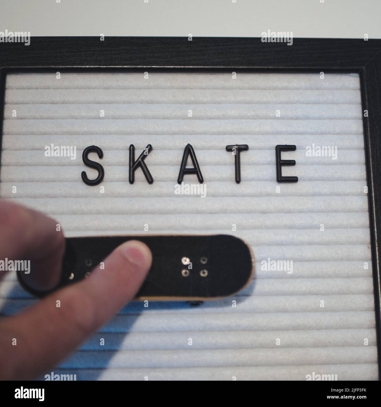 Skate in black text. Professional fingerboard expert about to do a 360 kickflip (tre flip). Fun graphic to illustrate skateboarding in a royalty free Stock Photo