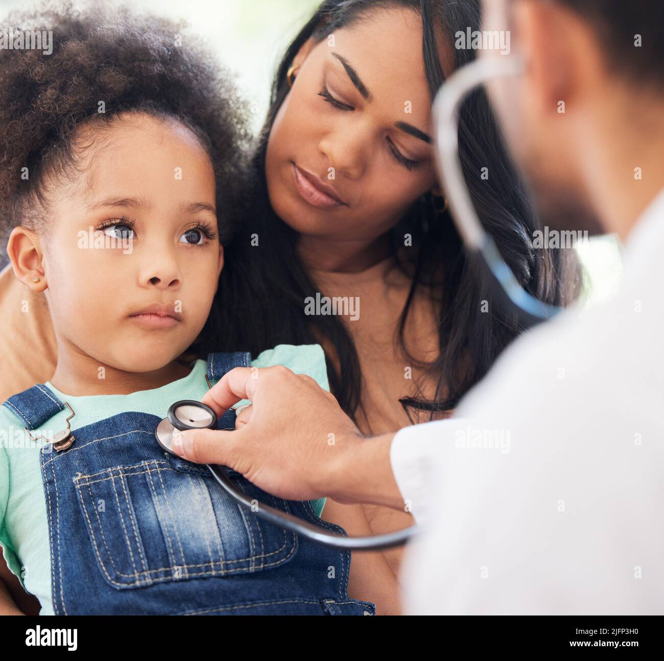 Lets take a look at your health. Shot of a little girl sitting on her mothers lap while being examined by her doctor. Stock Photo
