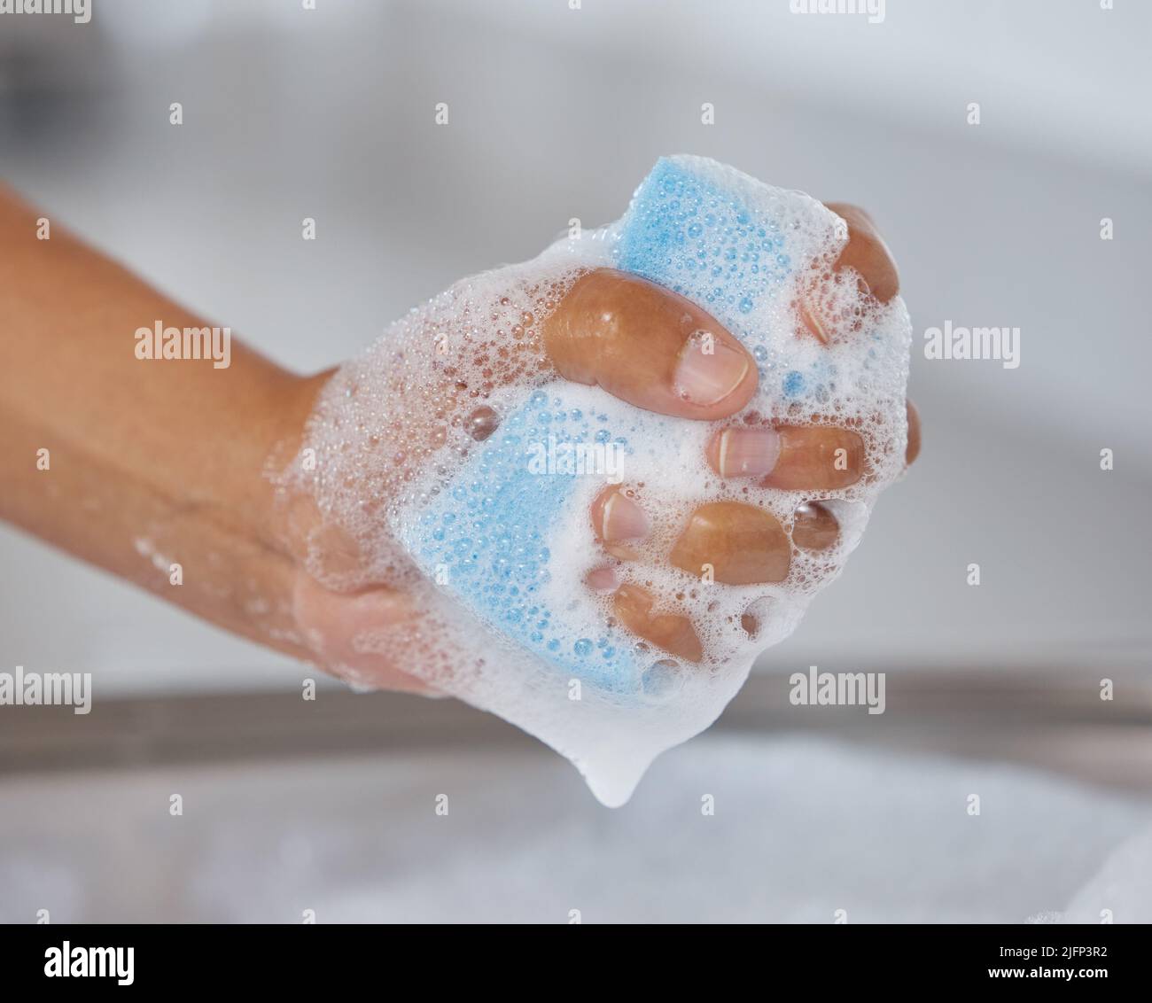 Time to tackle the dirty dishes. Closeup shot of an unrecognisable woman squeezing soap from a sponge at home. Stock Photo