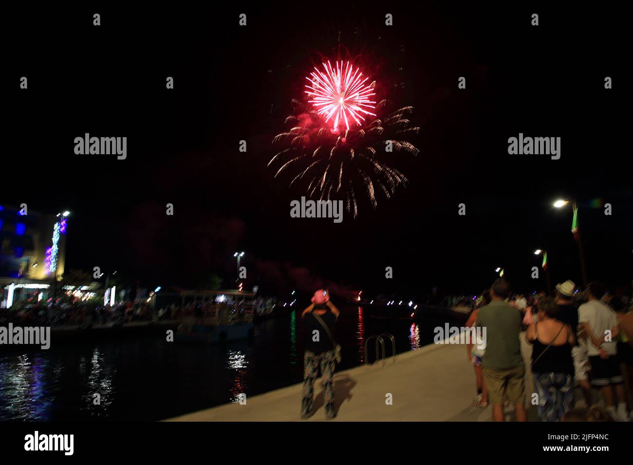 July 2, 2022, Bellaria Igea Marina, Rimini, Italy: Bellaria Igea Marina, Rimini, Italy - July 02, 2022 :Seen pink fireworks fired on the pier in the presence of tourists to start the Pink Night.The pink night is the New Year's Eve of summer, the main event of the Italian summer on the Riviera. Everything is tinged with pink and you can taste the sense of celebration that explodes from Ravenna to Cattolica in shows and concerts of national and international level.The rose is a color that calls to mind the sweetness, kindness and hospitality, which are the values that the Riviera wants to convey Stock Photo