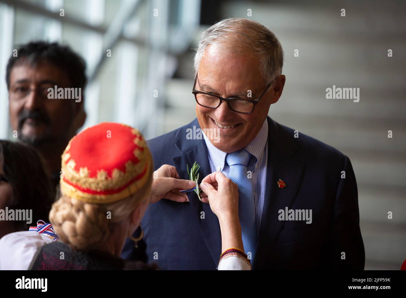 Seattle, Washington, USA. 4th July, 2022. Maria Plancich Kesovija, in traditional Croatian dress, pins a sprig of rosemary to the lapel of Washington Governor Jay Inslee during a naturalization ceremony at Fisher Pavilion. The U.S. Citizenship and Immigration Services and U.S. District Court for the Western District of Washington partnered with Seattle Center to host the annual ceremony welcoming 300 applicants from 74 countries as new citizens. Credit: Paul Christian Gordon/Alamy Live News Stock Photo