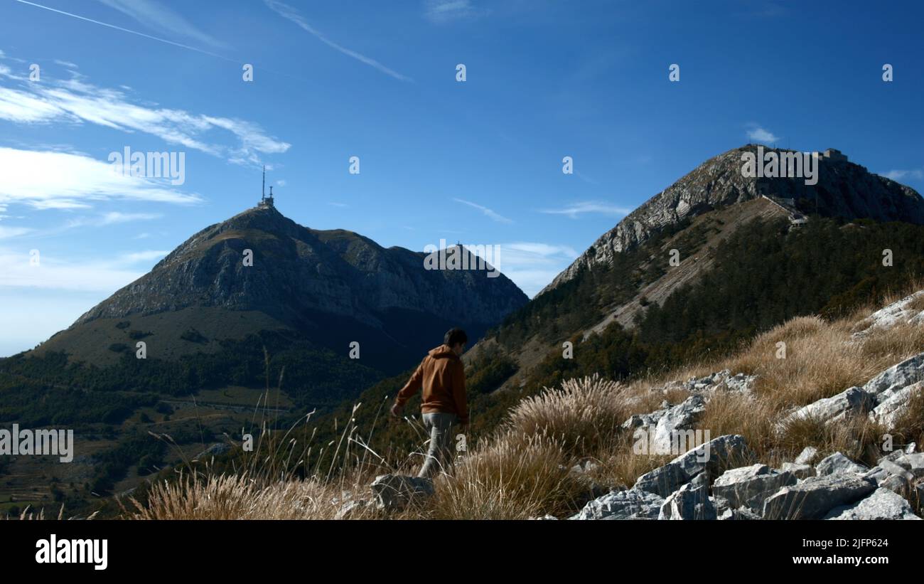 A man climbing the mountains.Creative.A young man who walks through the mountains on which monuments stand and green grass grows. Stock Photo