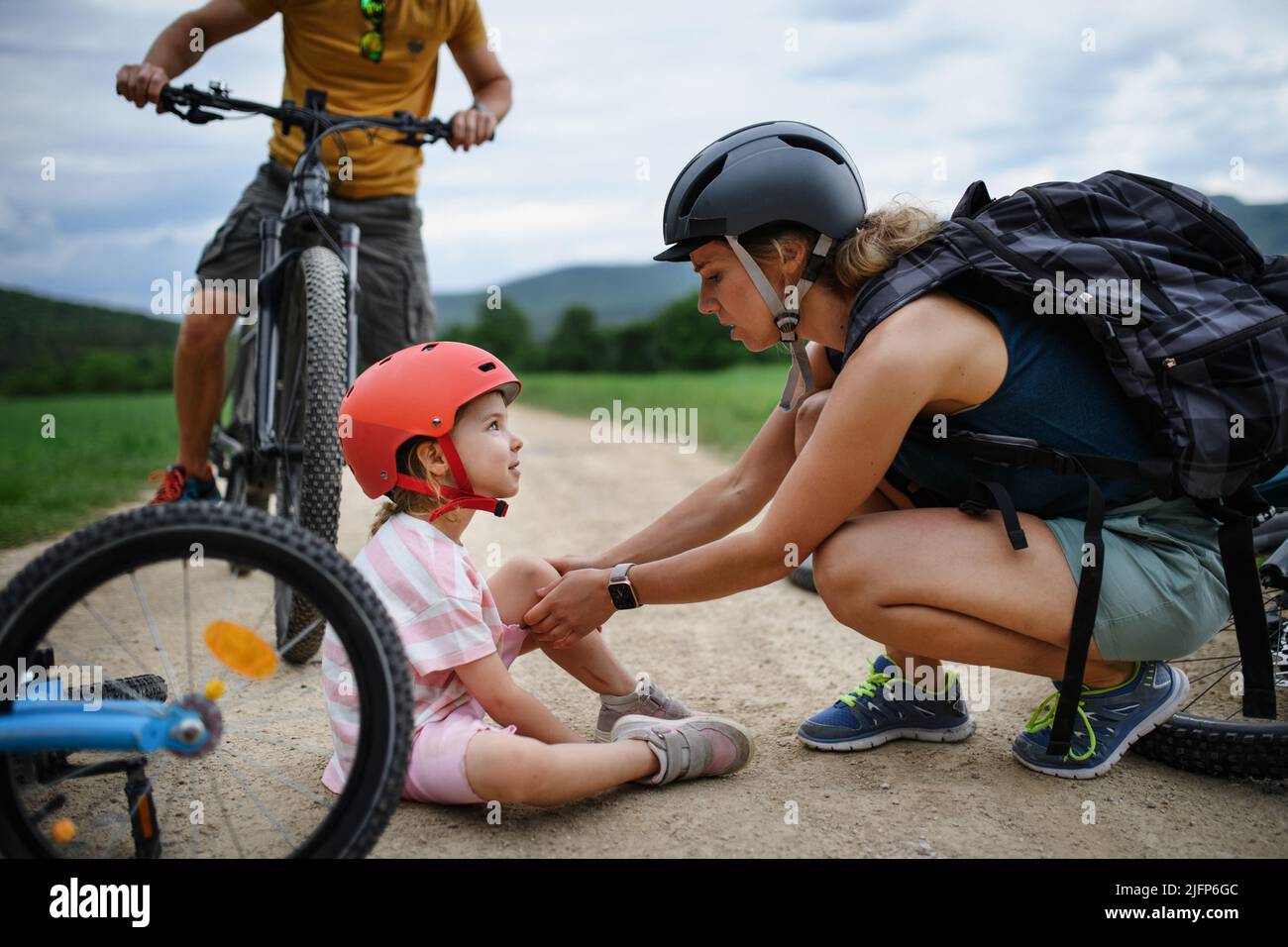 Mother and father helping their little daughter after falling off bicycle outdoors Stock Photo